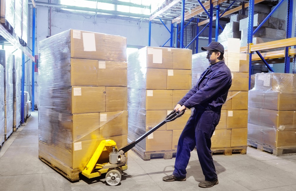 worker with fork pallet truck stacker in warehouse loading Group of cardboard boxes via pallet jack