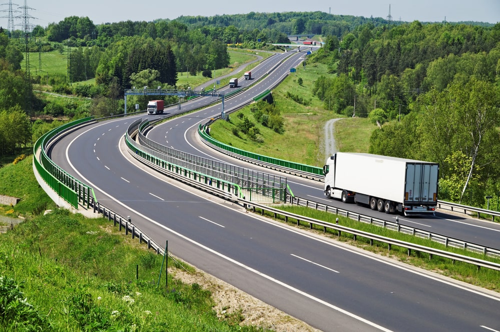 A truck moving through a green surrounding by road