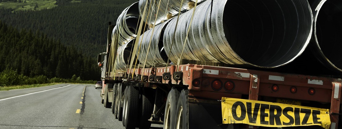 A truck hauling oversized pipes strapped to a flatbed trailer