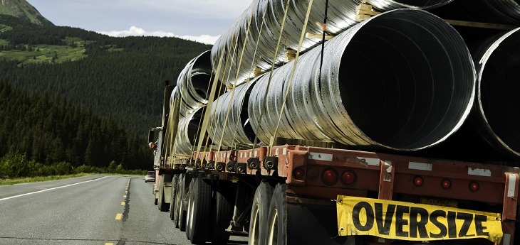 A truck hauling oversized pipes strapped to a flatbed trailer