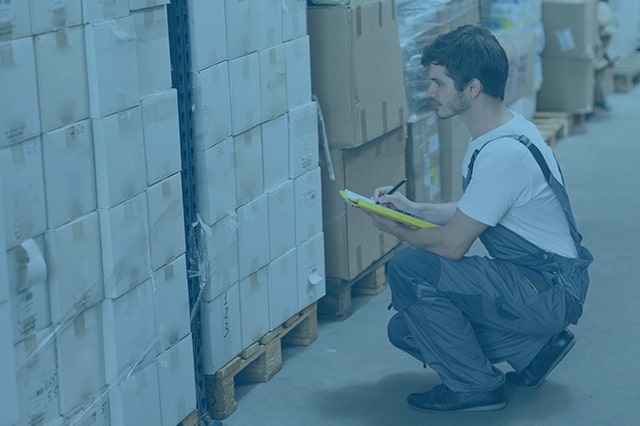 A dock worker taking notes next to a pallet stacked with boxes