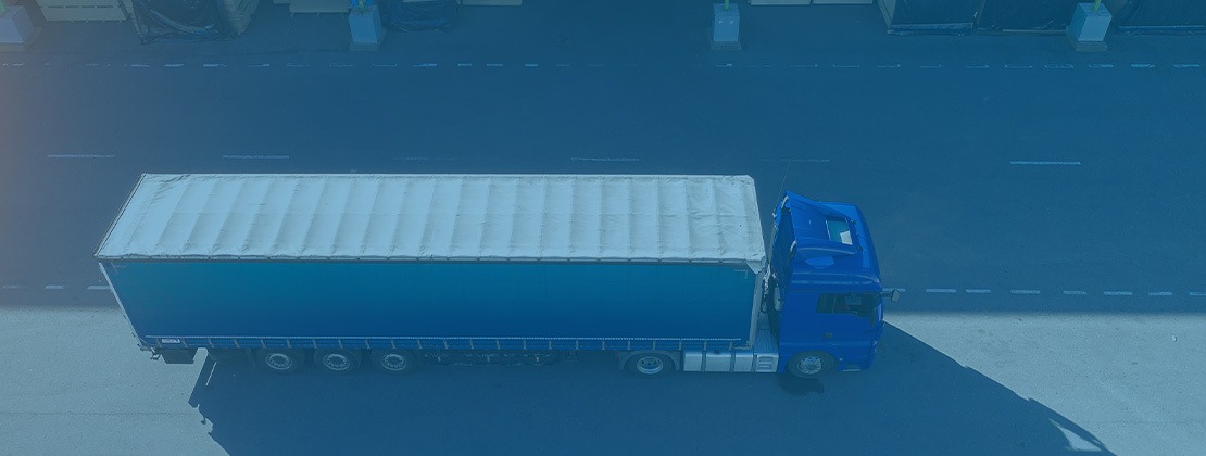A blue freight truck driving by a warehouse