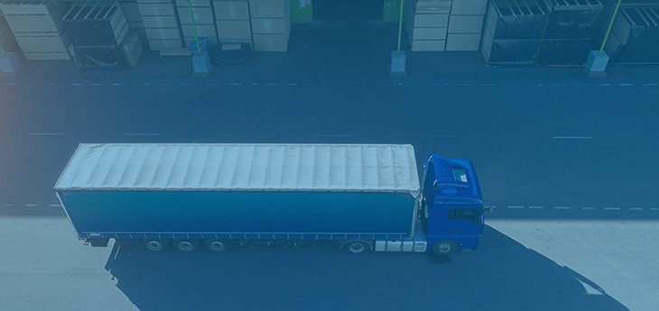 A blue freight truck driving by a warehouse