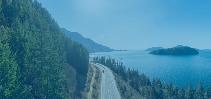 A truck traveling by road between the sea and a hillside