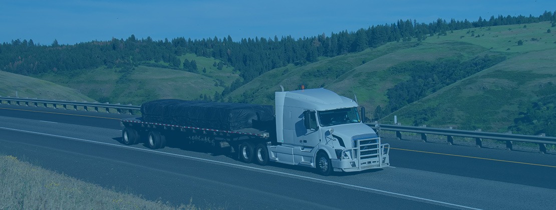 A flatbed truck transporting cargo on a road by a hillside