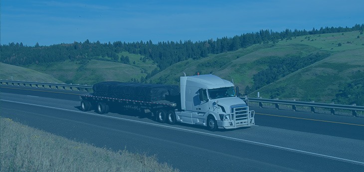 A flatbed truck transporting cargo on a road by a hillside