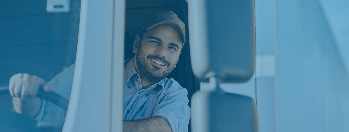A truck driver smiling from a tractor trailer.