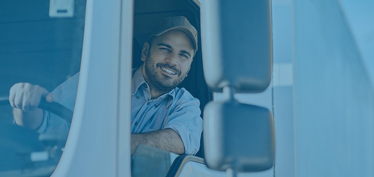 A truck driver smiling from a tractor trailer.