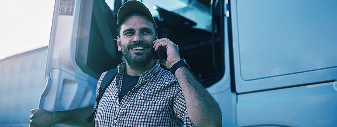 A truck driver getting off a truck, talking on the phone.