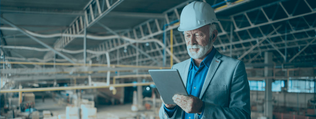 Older businessman wearing a hardhat is looking at a tablet.