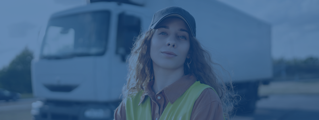 Female truck driver posing in a visibility vest next to a freight truck