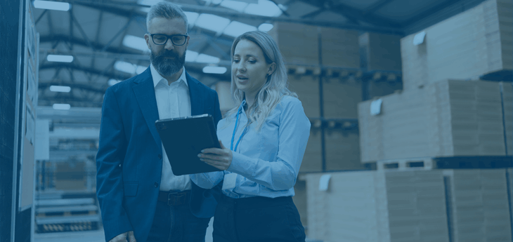 a businessman and businesswoman standing next to freight packages, looking at a clipboard.