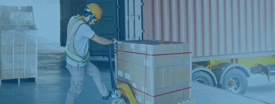 A warehouse worker moving a pallet using a pallet jack
